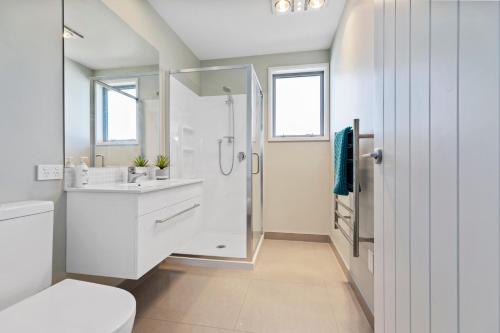 a white bathroom with a shower and a sink at Campbell Road Classic - Mount Maunganui Bach in Mount Maunganui