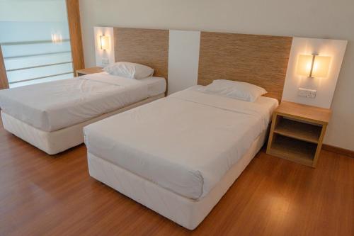 two beds in a hotel room with white sheets at The CEO Executive Suites in Bayan Lepas