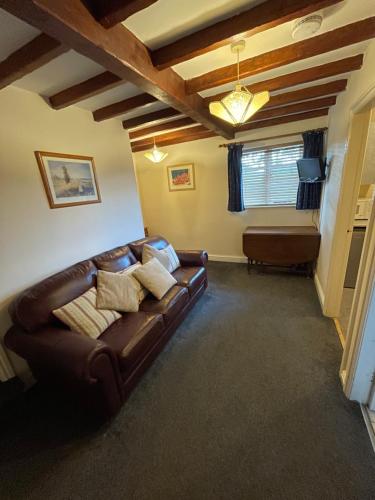 a living room with a brown leather couch and a window at Halfway House Inn & Cottages in Bridgnorth