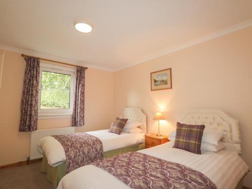 1 dormitorio con 2 camas y ventana en Garden Lodge en Muir of Ord