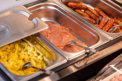 a buffet with a tray of breakfast foods and sausages at Hôtel de France Gare de Lyon Bastille in Paris