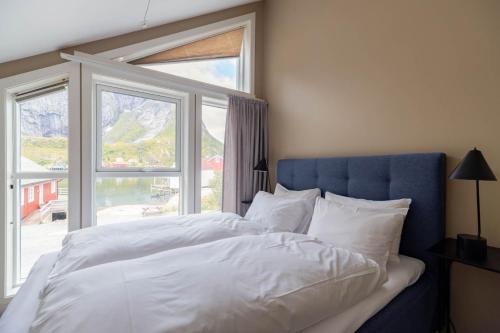 een slaapkamer met een bed met een blauw hoofdeinde en een raam bij May's Apartments by May's in Reine