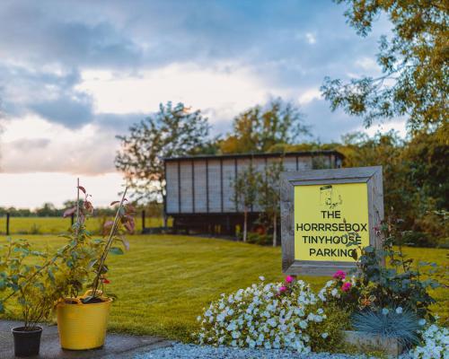 a sign in a yard with flowers and a building at The Horrrsebox Tinyhouse Glamping in Garadice