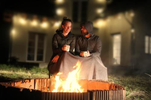 un homme et une femme assis à côté d'un feu dans l'établissement Kraniec Świata Unique Location Stylish Secured Parking Peace and Quiet Self Check-In, à Bolesławiec