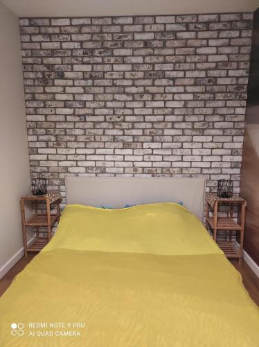 a bedroom with a yellow bed and a brick wall at Apartament na Wzgórzu Niebieski in Łańcut