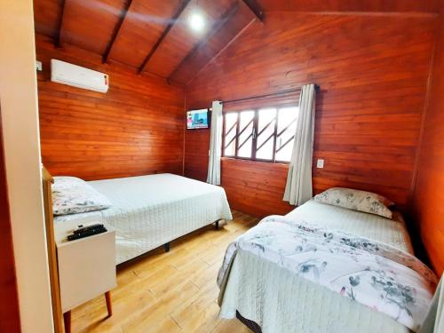 two beds in a room with wooden walls and a window at Pousada Morada dos Sonhos in Urubici