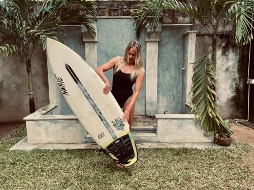 a woman is standing next to a surfboard at Midigama Holiday Inn in Midigama