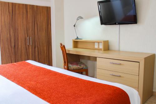 a bedroom with a bed and a desk with a television at Hotel & Suites Real del Lago in Villahermosa