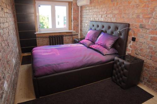 un letto in una camera in mattoni con lenzuola e cuscini viola di Mini cinema & movie studio with PS5 a Riga