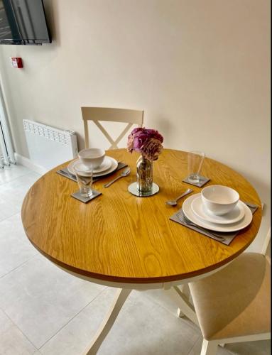 een houten tafel met borden en een vaas met bloemen erop bij Erne Getaway No.5 Brand new 1 bed apartment in Enniskillen