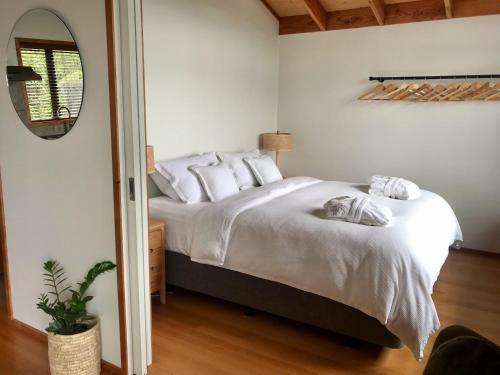 1 dormitorio con 1 cama con sábanas blancas y espejo en Adrift In Golden Bay- Absolute Beachfront Villas, en Collingwood
