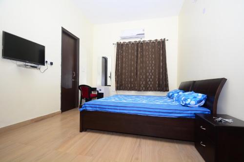 um quarto com uma cama com lençóis azuis e uma televisão de ecrã plano em Comfort Stay em Faridabad