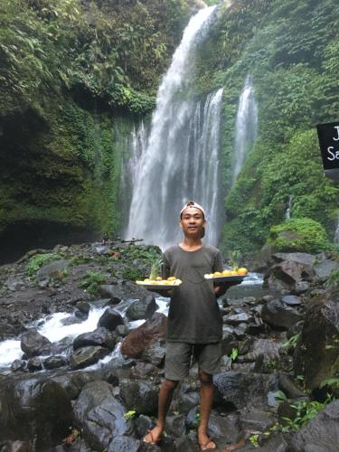 a man holding a tray of food in front of a waterfall at Rinjani Houseboon in Senaru