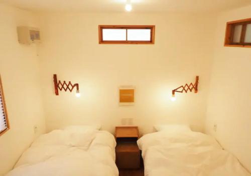 two beds in a room with white sheets and a window at とけとけ山荘 in Fujikawaguchiko