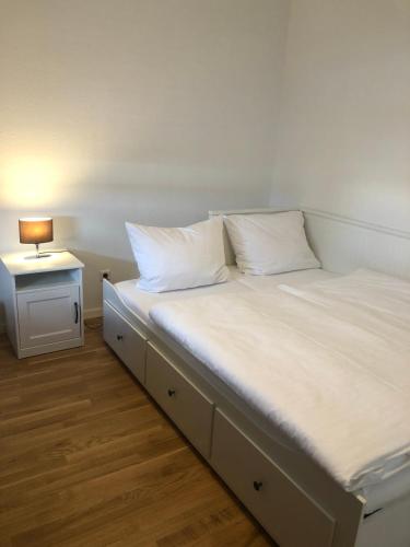 uma cama com lençóis brancos e uma mesa lateral com um candeeiro em Relax am Bodensee em Friedrichshafen