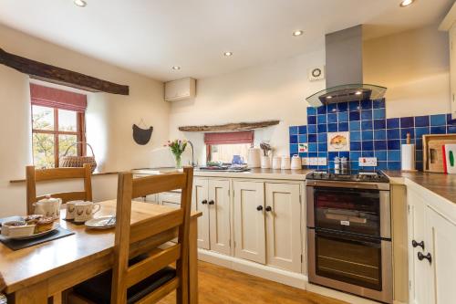 a kitchen with a wooden table and blue tiles on the wall at Holly Cottage in Honiton