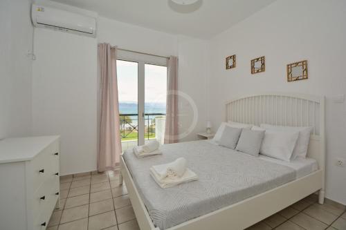 a white bedroom with a bed and a window at Vasiliki in Ermioni