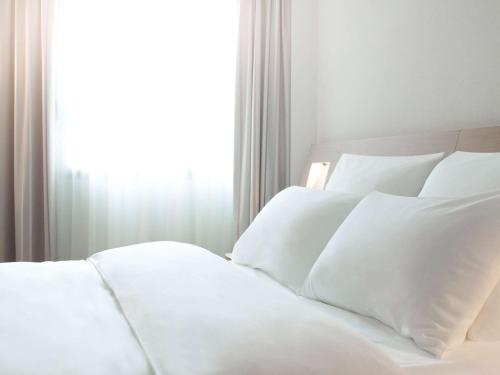 a white bed with white pillows in front of a window at Novotel Wolverhampton City Centre in Wolverhampton