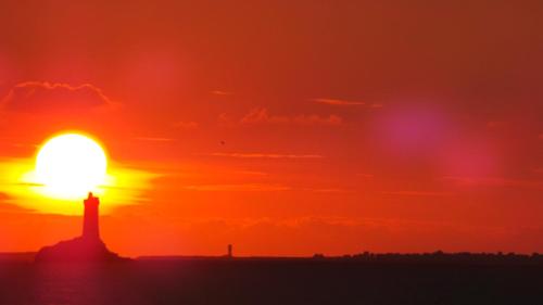 a sunset with a lighthouse in the foreground at Hôtel de la Baie des Trépassés in Plogoff