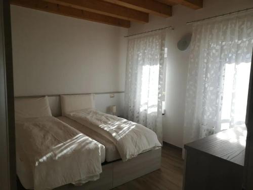 Schlafzimmer mit einem Bett mit weißer Bettwäsche und Fenstern in der Unterkunft Cadore Luminoso appartamento in Calalzo