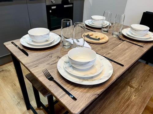 a wooden table with plates and bowls and wine glasses at Perfect 1 Bed Apartment - Central with Parking, WiFi, TV, Desk in Peterborough