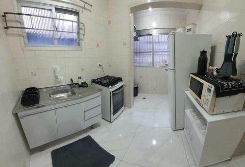 a white kitchen with a sink and a refrigerator at SOL & MAR I com VARANDA - 1 dormitório - Canto do FORTE - 300 m da Praia e 20m da Avenida dos Barzinhos - ESTACIONAMENTO gratuito e WI Fi 300mbytes com TV a cabo - ap113 in Praia Grande