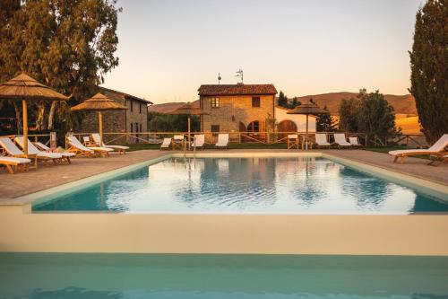 a swimming pool with chairs and a house in the background at Le Fraine - Agriturismo & Olives Glamping in Santa Luce