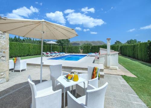 a patio with a table with an umbrella and a pool at Owl Booking Villa Tofol - Ideal For Family and Friends in Pollença