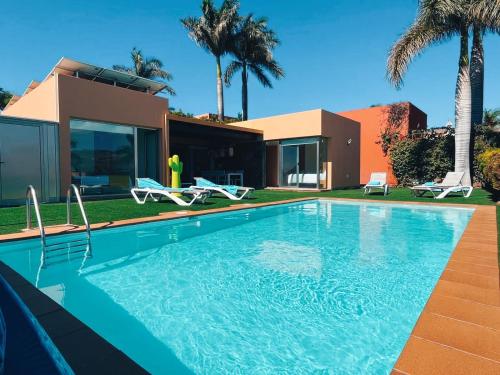 a swimming pool in front of a house with palm trees at Villa Lía by SunHousesCanarias in Salobre
