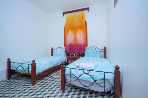two twin beds in a room with a window at Hotel TOURAGHINE in Chefchaouene
