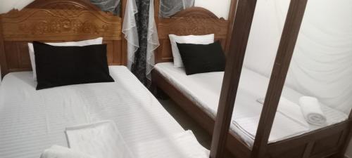 Habitación con 2 camas individuales, sábanas blancas y almohadas negras. en Lyneks Cosy Apartment, en Mombasa