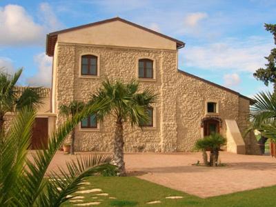 a large stone house with a palm tree in front of it at Corte dei Monaci in Canicattì