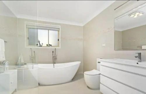 baño blanco con bañera, aseo y lavamanos en Neogaia Bed & Breakfast, en Beecroft