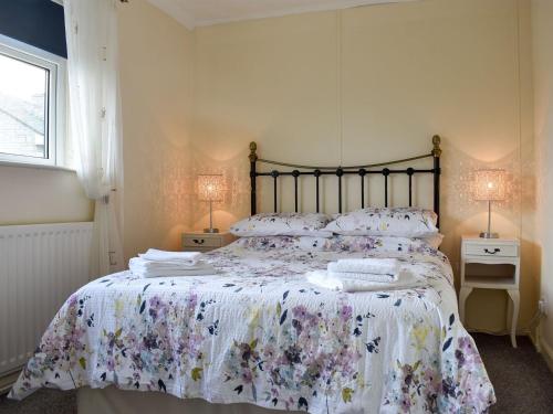 a bedroom with a bed with a floral bedspread and two lamps at Cotswolds Cottage in Hamsterley