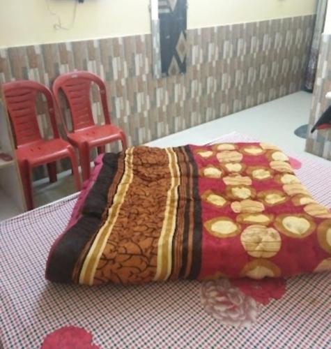 a bed with a blanket and two red chairs at Panna Tiger Home Stay in Khajurāho