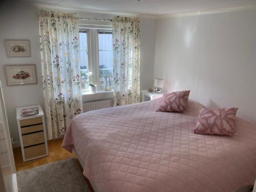 1 dormitorio con cama con sábanas rosas y ventana en Bekvämt boende mitt i gamla genuina Skärhamn en Skärhamn