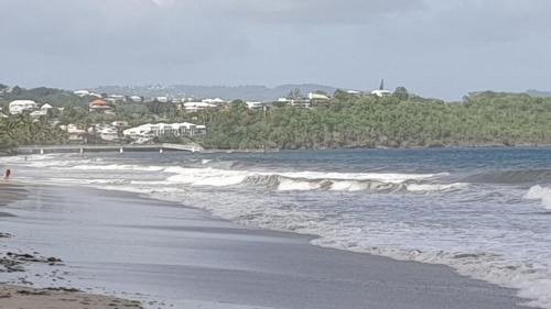 a beach with waves and buildings in the background at Ti'Krystal in Le Diamant