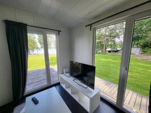 ein Wohnzimmer mit einem Flachbild-TV und großen Fenstern in der Unterkunft Mökki Vanajaveden rannalla Kirstulan Kartanossa in Hämeenlinna