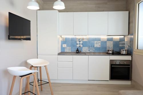 a kitchen with white cabinets and a tv and stool at Pescoluse Apartments in Marina di Pescoluse