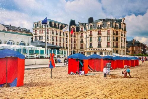- une plage avec des tentes rouges et bleues et un bâtiment dans l'établissement Appartement FACE MER accès direct plage, à Houlgate
