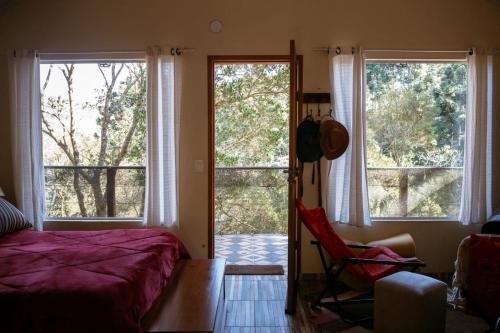 a bedroom with a bed and two large windows at Chalé da Mata in Sapucaí-Mirim