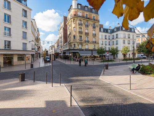 a city street with buildings and people sitting on a bench at Appartement au centre de Vincennes in Vincennes