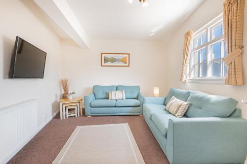 a living room with two blue couches and a tv at Cottage 9 Old Farmhouse Braithwaite in Keswick