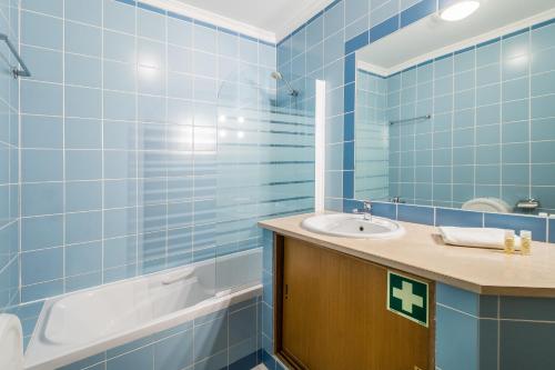 a blue tiled bathroom with a sink and a tub at Jardins Meia Praia 104 by Algarve Golden Properties in Lagos