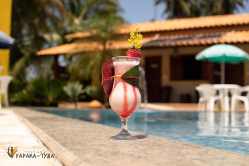 a drink with a strawberry in a glass next to a swimming pool at Pousada Yapara-Tyba in Japaratinga