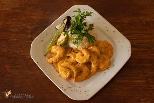 a white plate with shrimp and vegetables on a table at Pousada Yapara-Tyba in Japaratinga