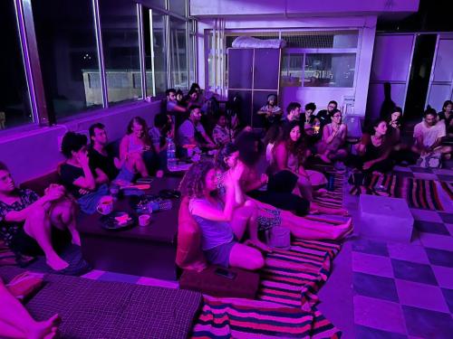 Tatsat Hostel في ريشيكيش: مجموعة من الناس يجلسون في غرفة ذات أضواء أرجوانية