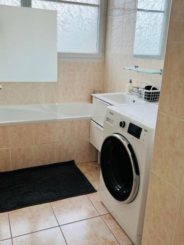 La salle de bains est pourvue d'un lave-linge blanc et d'une baignoire. dans l'établissement Superbe Appartement lumineux proche Disney, à Montévrain