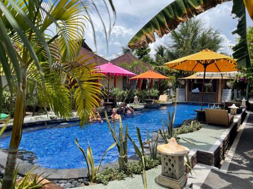 a swimming pool with people sitting in chairs and umbrellas at Banana cottages in Gili Air