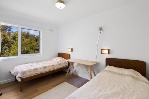 two beds in a room with a table and a window at Myrtle Cottage in Aireys Inlet